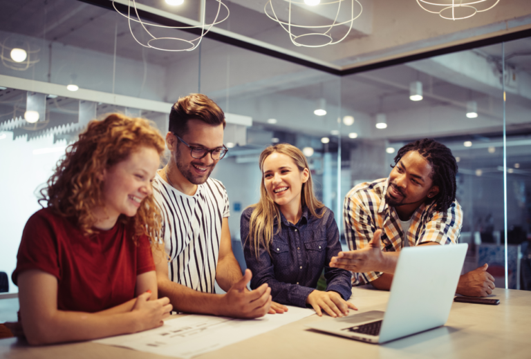 photo of 4 smiling people in an office working on a project on a laptop