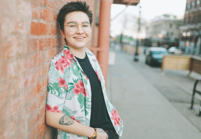 Photo of a young trans man standing by a brick wall